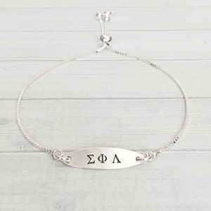 May include: A silver adjustable bracelet with a silver oval charm that says "ΣΦΛ".