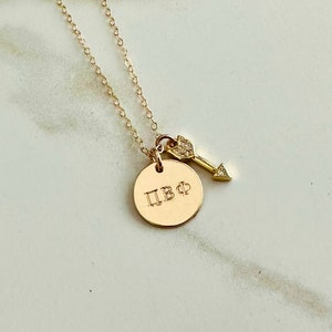 May include: Gold necklace with a round pendant engraved with the letters "ПВФ" and a small arrow charm with a single diamond accent.