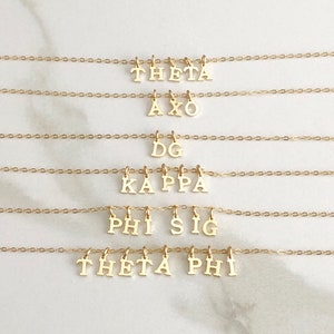 May include: Five gold necklaces with different Greek letter sorority names hanging from them. The names are Theta, AXO, DG, Kappa, Phi Sig, and Theta Phi.