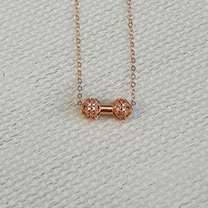 Peut inclure: Un collier en or d&eacute;licat avec un petit pendentif rond &agrave; motif textur&eacute;. Le pendentif est compos&eacute; de deux sph&egrave;res reli&eacute;es.