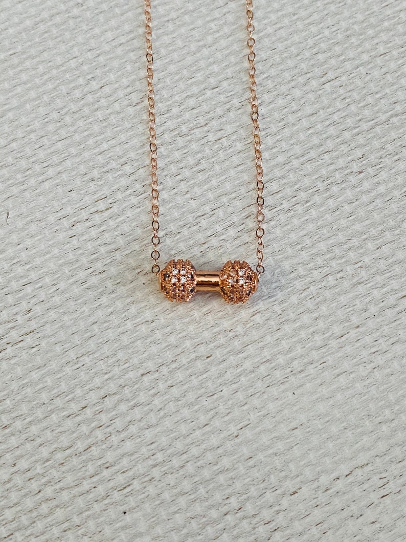 Peut inclure: Un collier en or d&eacute;licat avec un petit pendentif rond &agrave; motif textur&eacute;. Le pendentif est compos&eacute; de deux sph&egrave;res reli&eacute;es.