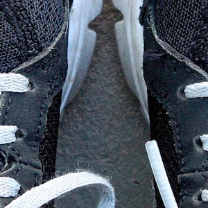 May include: A pair of black sneakers with white laces. The left shoe has a silver tag that reads "She believed she could". The right shoe has a silver tag that reads "So she did".