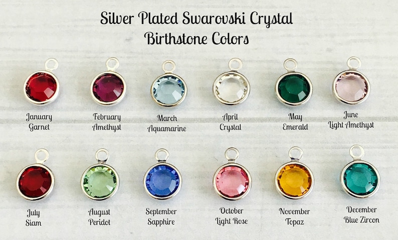 May include: Twelve silver-plated charms with Swarovski crystals in different colors, representing the birthstones for each month of the year. The charms are arranged in two rows of six, with the month and birthstone name listed below each charm.