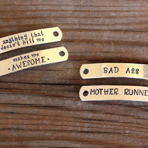 May include: Four silver metal tags with different sayings on them. The tags read "anything that doesn't kill me makes me AWESOME", "BAD A$$", and "MOTHER RUNNER".