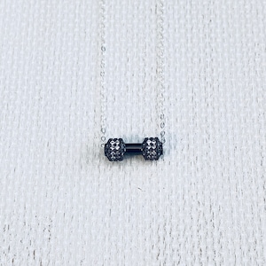 Peut inclure: Un collier en cha&icirc;ne argent&eacute;e avec un pendentif en forme d'halt&egrave;re noir. L'halt&egrave;re est recouvert de petits cristaux transparents.