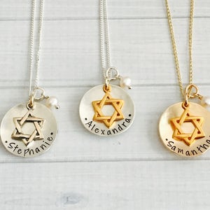 May include: Three silver necklaces with a gold Star of David charm and a small pearl accent. The charms are engraved with the names "Stephanie", "Alexandra", and "Samantha".