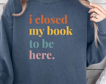May include: A navy blue sweatshirt with the text "i closed my book to be here." in rainbow colors.