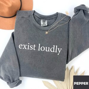 May include: A charcoal gray sweatshirt with the text "exist loudly" printed in white on the front.