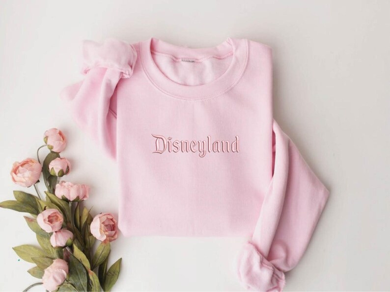 May include: A pink sweatshirt with the word "Disneyland" embroidered in a cursive font on the front.