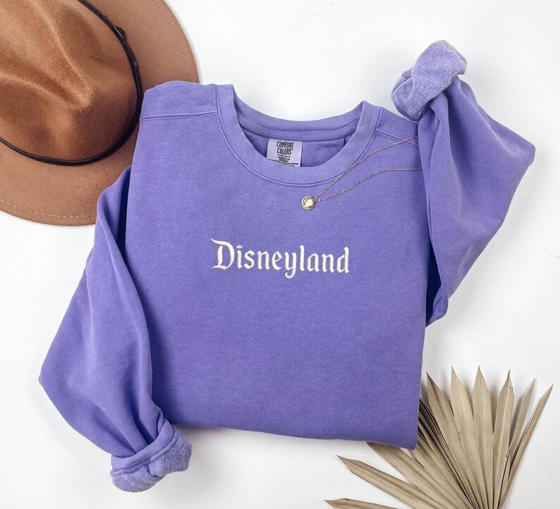 May include: Purple sweatshirt with the text "Disneyland" embroidered in white on the front.