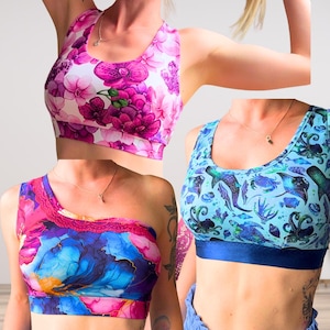 May include: Three athletic crop tops featuring distinct patterns: one with a vibrant pink orchid floral print, one with a blue and purple abstract marble design with lace trim, and one with a light blue aquatic print of sea creatures.