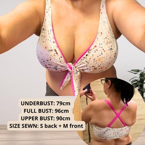 Könnte beinhalten: Weißes Bikini-Oberteil mit farbenfrohem Spritzmuster und rosa Besatz. Das Oberteil wird vorne gebunden und hat einen passenden Rücken. Maße: Unterbrustumfang 79cm, Brustumfang 96cm, Oberbrustumfang 90cm. Genähte Größe: S hinten + M vorne.