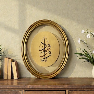 May include: A gold framed oval wall art piece with Arabic calligraphy on a tan background. The artwork is displayed on a wooden dresser, with decorative vases, books, and flowers. The frame has a gold finish.