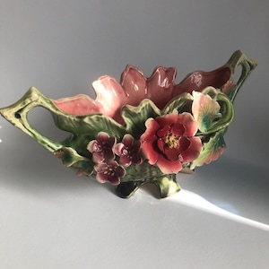 Pode incluir: Uma tigela de cerâmica com um design floral. A tigela tem a forma de uma folha e duas alças. A tigela é decorada com flores rosa, vermelhas e verdes.