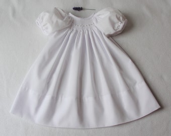 May include: A white smocked dress with puffed sleeves and a gathered skirt. The dress is made of a soft, lightweight fabric and has a simple, elegant design.