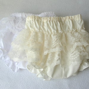 May include: Two pairs of ruffled lace bloomers. One pair is white and the other is ivory.