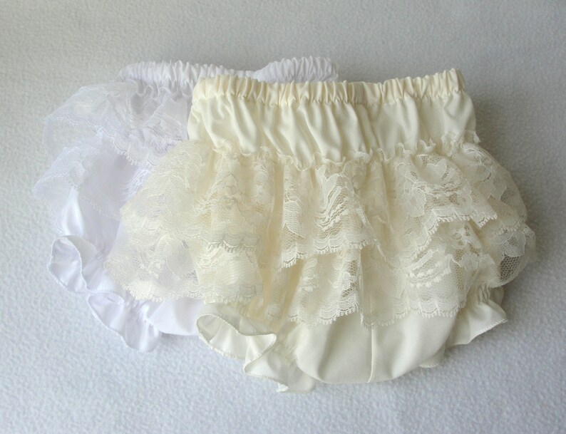 May include: Two pairs of ruffled lace bloomers. One pair is white and the other is ivory.