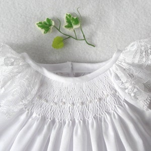 May include: White baby dress with a smocked bodice and lace trim on the sleeves.