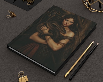 May include: A black leather-bound journal with a dark, moody image of a woman with long dark hair holding a snake. The image is set in a dark forest with vines and leaves.