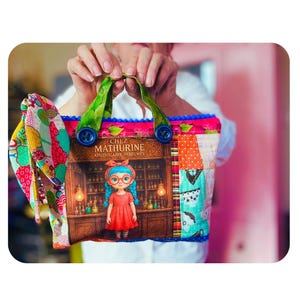 Peut inclure: Un sac à main en tissu matelassé avec un panneau central illustrant une fille en robe rouge dans une boutique marquée CHEZ MATHURINE APOTHICAIRE PARFUMES. Le sac possède des anses vertes à motifs, des boutons bleus et un nœud latéral à motifs floraux.