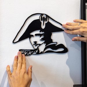 Puede incluir: Una silueta en blanco y negro de una persona que lleva un sombrero con una cruz en la parte superior. La silueta está montada en una pared blanca.