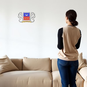 Könnte beinhalten: Eine Frau steht vor einer weißen Wand mit einem Sofa im Vordergrund. An der Wand befindet sich ein Wappen mit einer Mondsichel, zwei Sternen und zwei Seepferdchen.