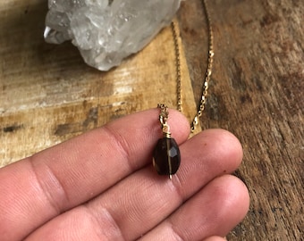 May include: A gold chain necklace with a dark brown gemstone pendant.