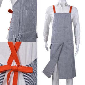 May include: A blue and white striped apron with orange straps and ties. The apron has a front pocket and a split design on the lower front. The straps cross in the back and tie at the waist. The apron is displayed on a mannequin.