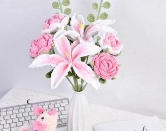 May include: A bouquet of crocheted pink and white flowers in a white vase. The flowers are lilies and roses. The bouquet is on a white table with a keyboard and a crocheted pig toy.