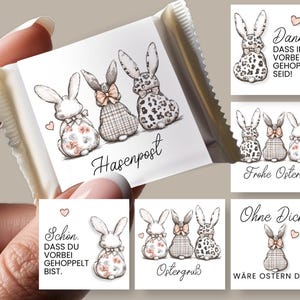 Könnte beinhalten: Eine verpackte Schokoriegel mit einem weißen Etikett mit drei skizzierten Hasen mit gemusterten Schleifen und floralen Akzenten. Der Text "Hasenpost" ist kursiv geschrieben. Zusätzliche Karten mit Hasenillustrationen und deutschem Text.