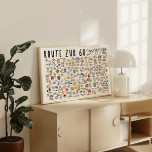 May include: A framed print with the text "ROUTE ZUR 60" and "GEBOREN 1966" in black. The print features numerous hand-drawn icons and stars, with a cream-colored background. The frame is a light wood color.