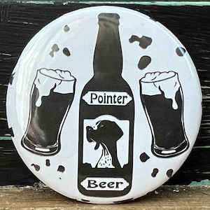 May include: White round button featuring a black and white illustration of a beer bottle, two beer glasses, and a dog. The beer bottle is labelled "Pointer Beer".