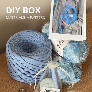 Peut inclure: Un kit de bricolage pour le crochet avec du fil bleu clair, un petit sac à main bleu et un sac transparent contenant des crochets et des accessoires. Le texte "DIY BOX MATERIALS + PATTERN" est visible. Disponible en 4 couleurs.