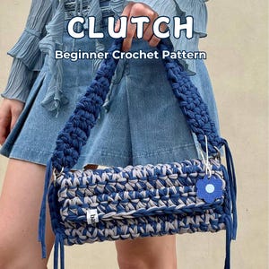 Puede incluir: Un bolso de mano de ganchillo azul y gris con un charm de flor azul. El bolso tiene un asa trenzada y las palabras "CLUTCH" y "Beginner Crochet Pattern" se muestran en la imagen.