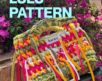 May include: A handmade crochet handbag featuring a vibrant color palette of olive green, bright pink, yellow, and white fabric strips. The bag includes integrated handles and decorative hanging fabric fringe, with a white label reading barwy.
