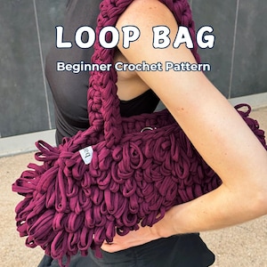 May include: A deep burgundy crochet bag featuring a textured loop design and a thick handle. The text LOOP BAG Beginner Crochet Pattern is overlaid on the image. The bag is constructed from thick fabric yarn with a small white brand tag attached.