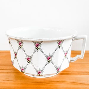 May include: A white ceramic mug with a black handle and the text "But First, Coffee" in a bold, black font. The mug is set against a blurred background, suggesting a cozy setting. The mug appears to be 12 ounces.