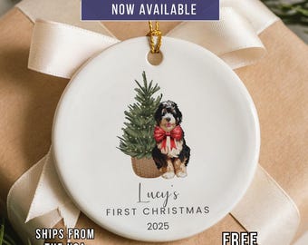 May include: A white ceramic Christmas ornament with a gold string. The ornament features a watercolor illustration of a dog with a red bow, a Christmas tree, and the text "Lucy's First Christmas 2025". The text "Custom Photo Option Now Available" is at the top.