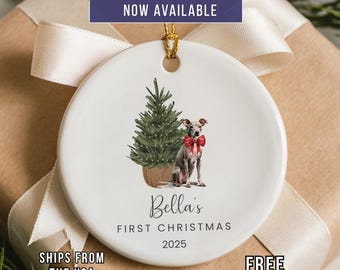 May include: White ceramic Christmas ornament with a gold string. The ornament features a watercolor illustration of a dog wearing a red bow, a Christmas tree, and the text "Bella's First Christmas 2025". The text "Custom Photo Option Now Available" is at the top.
