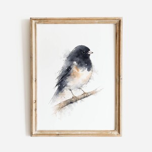 May include: Watercolor painting of a small bird with black, gray, and tan feathers perched on a branch. The bird is set against a white background, framed in a light brown wooden frame. The artwork has a soft, artistic style.