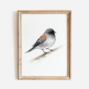 May include: Watercolor painting of a small bird perched on a branch, set in a wooden frame. The bird features gray, white, and brown tones, with a black beak and eye. The artwork has a minimalist style and is set against a white background.