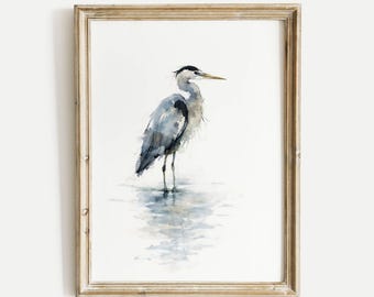 May include: Watercolor painting of a Great Blue Heron in a distressed gold frame. The bird is depicted in shades of gray and blue, standing in water. The artwork has a serene, natural theme, suitable for home decor.