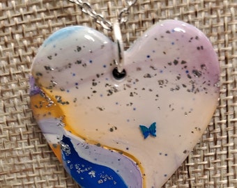 Corazón de arcilla polimérica hecha a mano en azul, blanco y naranja con mariposa azul y collar de brillo plateado