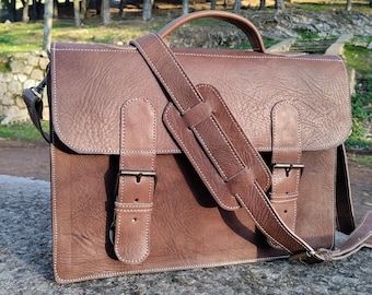 May include: A brown leather briefcase with a shoulder strap and two buckles. The bag has a textured surface and a stitched design.