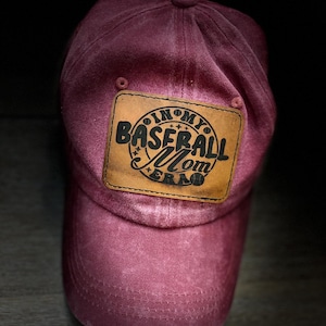 May include: A maroon baseball cap with a brown leather patch that says "In My Baseball Mom Era".