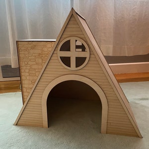 May include: A wooden dog house shaped like a triangular A-frame with a round window and a stone-patterned side panel.