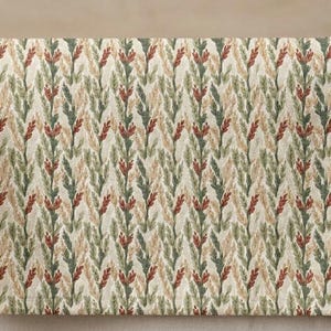 Puede incluir: Textil rectangular con un patrón repetido de hojas estilizadas en tonos verdes, beige y rojos. La tela está drapeada sobre una barra de madera y una superficie de color neutro.