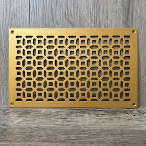 Può includere: Una griglia di ventilazione rettangolare in metallo color oro caratterizzata da un motivo geometrico ripetitivo di quadrati e ottagoni. La piastra piatta presenta quattro piccoli fori circolari per viti, uno in ogni angolo, per il fissaggio.