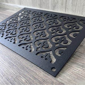 Peut inclure: Une grille d'aération rectangulaire en métal noir présentant un motif répétitif découpé au laser de fleurs de lys stylisées. Le panneau plat possède une finition mate texturée et comprend de petits trous de fixation circulaires aux coins.