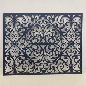 Può includere: Un pannello rettangolare in metallo nero caratterizzato da un intricato design tagliato al laser con viticci simmetrici e motivi floreali. La lastra piatta presenta piccoli fori di montaggio circolari agli angoli.